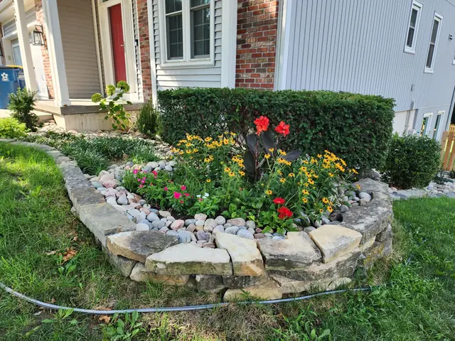 Raised planting bed built from natural stone, filled with river rock and summer flowers.