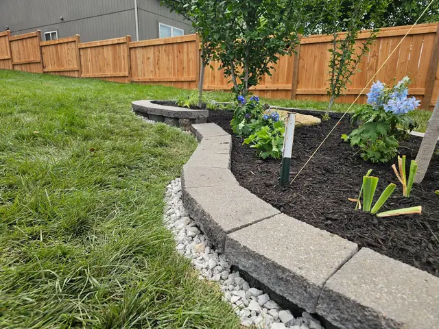 Curved stone-edged planting bed with a white river-rock border and new hydrangeas.