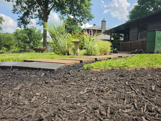 Stone paver walkway running beside a freshly mulched bed with ornamental grasses.