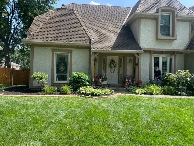 Front-yard planting beds with stone edging and a freshly mown lawn.